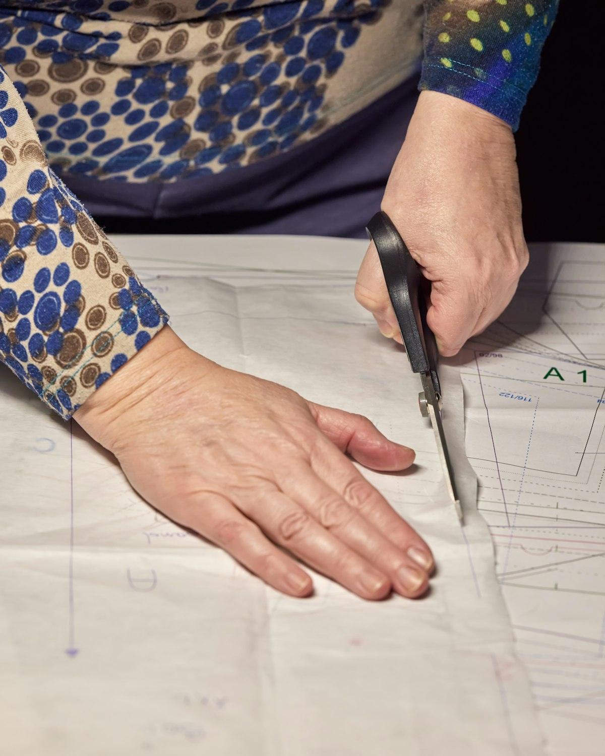 Hands cutting out a paper sewing pattern with scissors